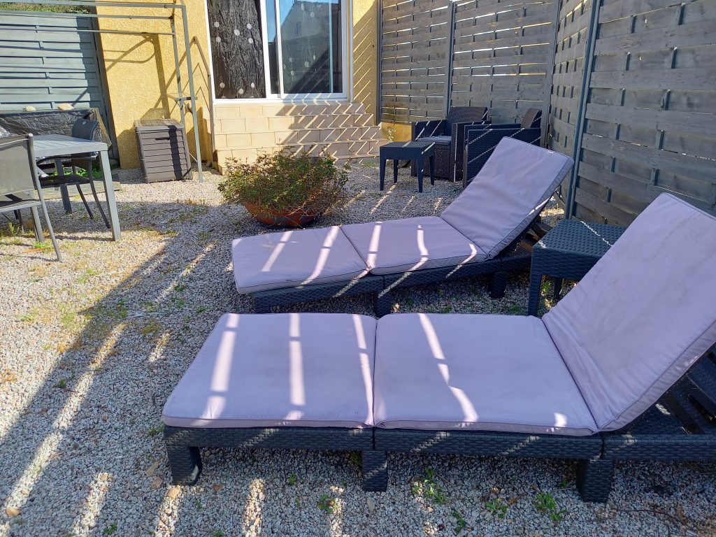 Photo qui représente l'espace jardin privatif de Mèrula, composé d'une table de jardin, d'un salon et deux transats avec un parasol et d'une plancha