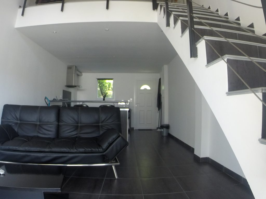 Photo qui représente l'espace salon de Mèrula où l'on peut apercevoir la cuisine équipée et l'escalier qui mène à la chambre et à la salle de bain